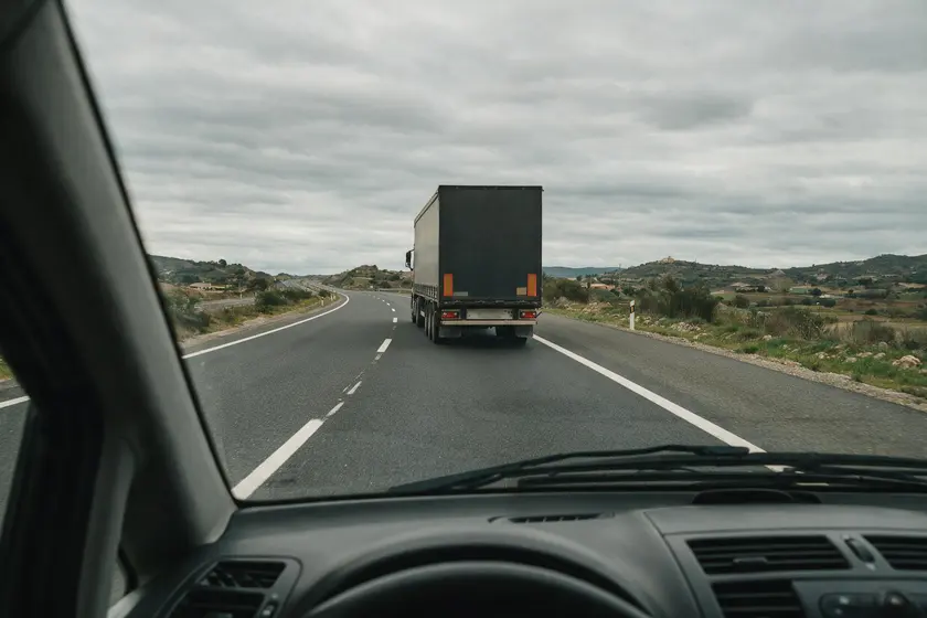 Carretera convencional vista desde el puesto del conductor, con la parte trasera de un camión articulado circulando delante en el mismo carril