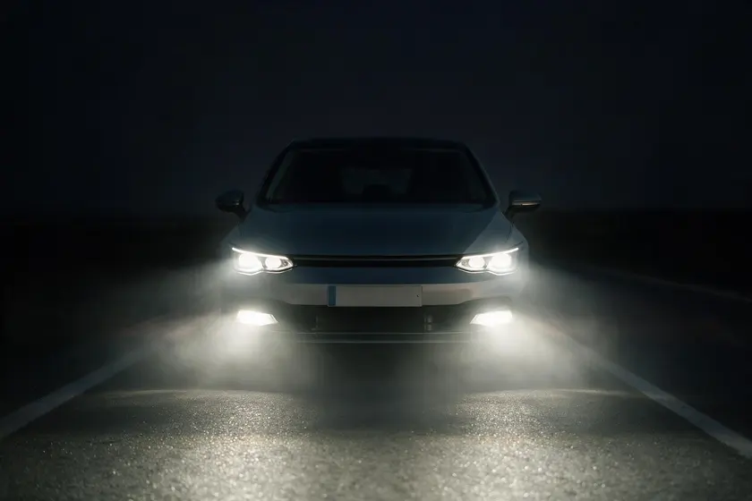 Coche de noche visto de frente con la luz de cruce y las dos luces antiniebla delanteras encendidas, con niebla ligera