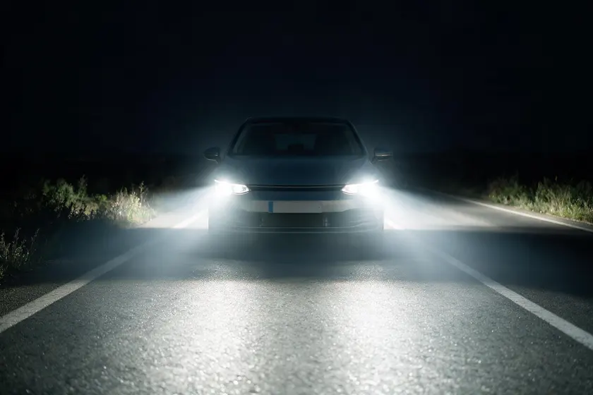Coche de noche visto de frente con la luz de carretera encendida, iluminando la calzada a mucha distancia