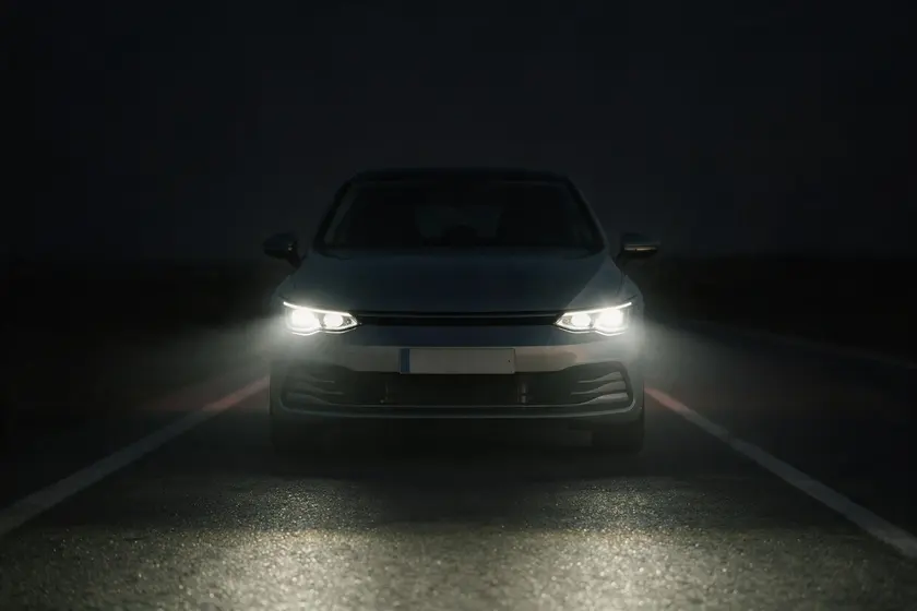Coche de noche visto de frente con la luz de cruce encendida, iluminando el asfalto por delante sin deslumbrar