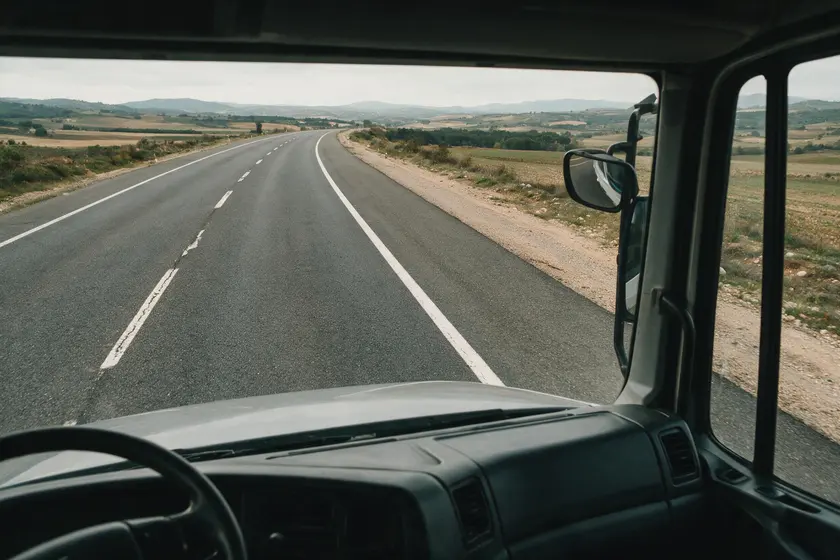 Carretera convencional vista desde la cabina de un camión, con un carril por sentido, arcén y el capó del camión en primer plano