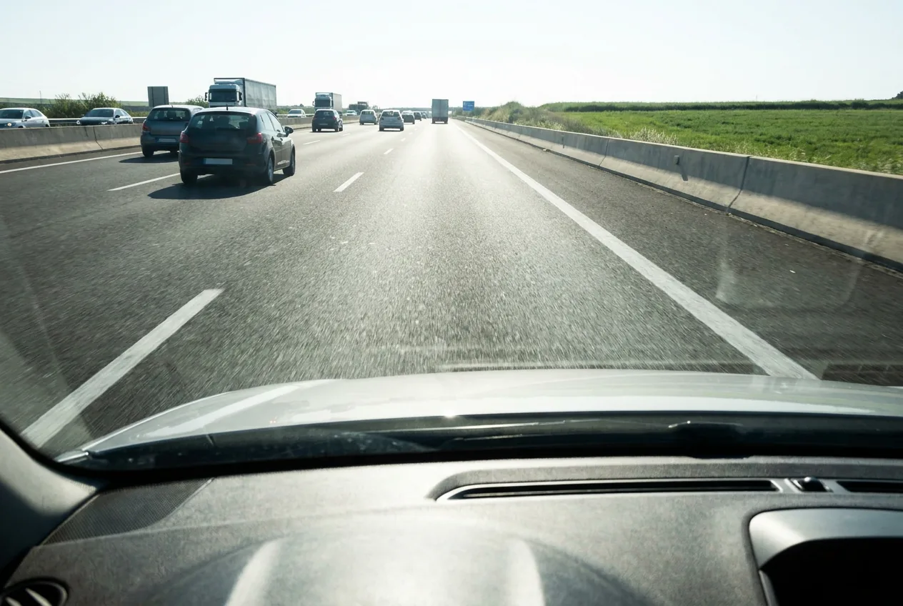 Vista desde el interior de un coche circulando por el carril de aceleración de una autovía, delimitado por líneas blancas a ambos lados, con el tráfico de la calzada principal a la izquierda