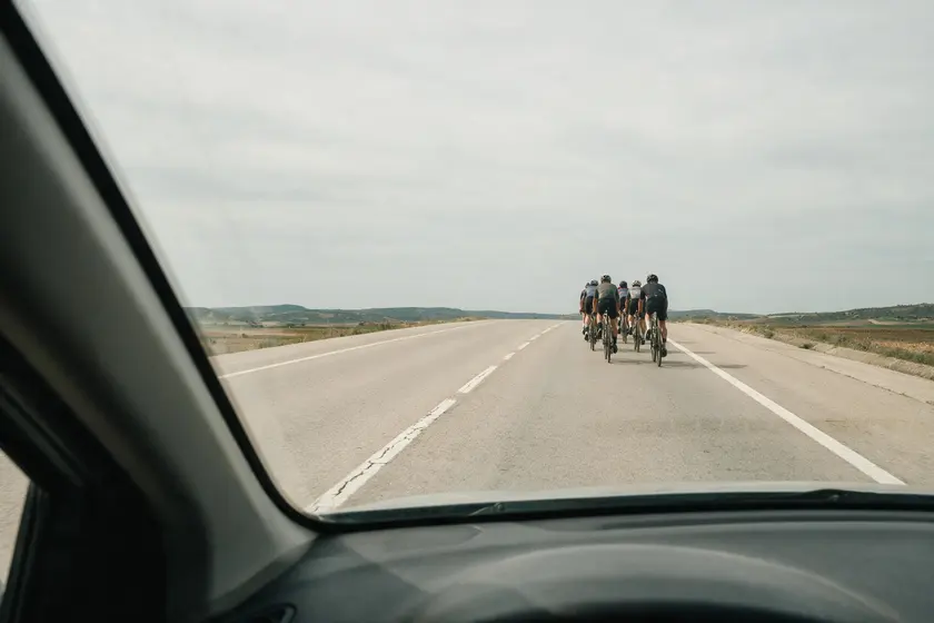 Grupo de ciclistas circulando por delante en una carretera convencional, visto desde el puesto del conductor