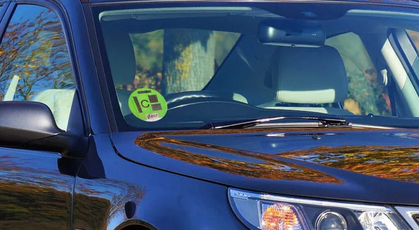 Foto real de un distintivo ambiental C (verde) de la DGT pegado en el ángulo inferior del parabrisas de un coche