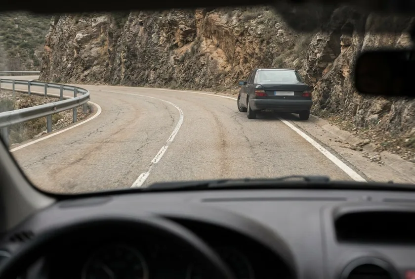 Vista desde el interior de un coche de una carretera de montaña con un turismo detenido junto a la roca, en plena curva de visibilidad reducida