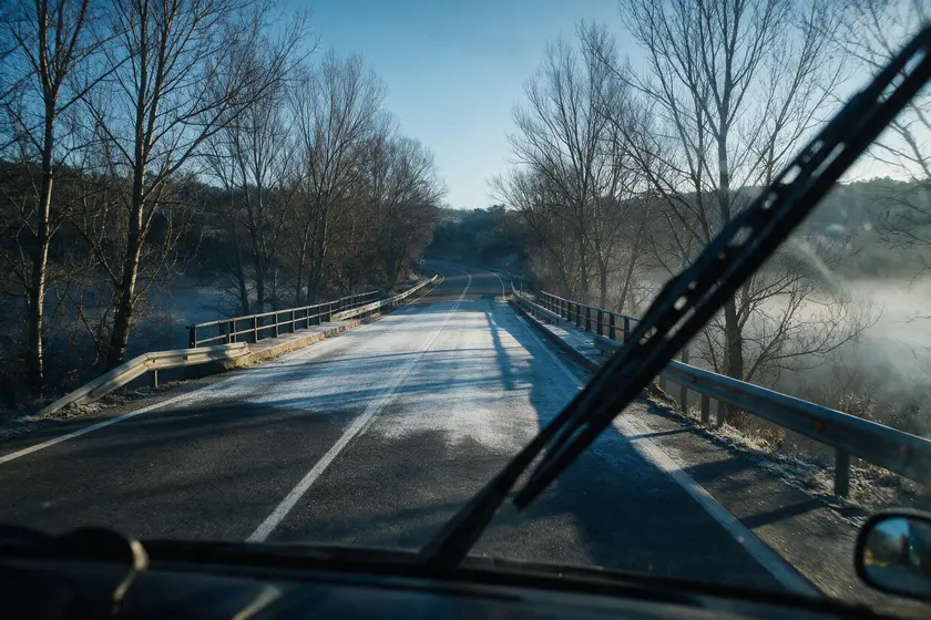 Puente y tramo en sombra con la calzada cubierta de escarcha, más clara que el asfalto seco al sol