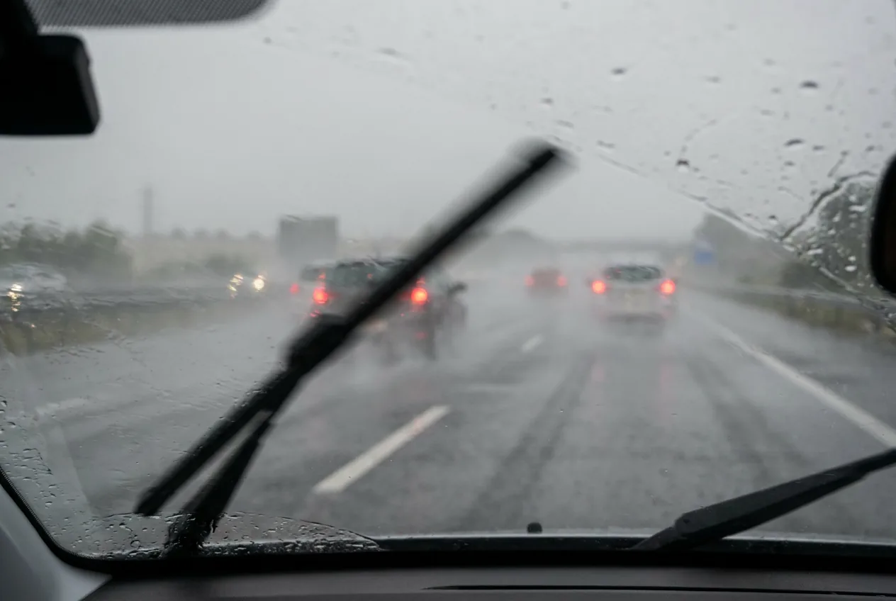 Vista desde el interior de un coche en una autovía bajo lluvia muy intensa, con el agua levantada por el tráfico reduciendo mucho la visibilidad y los pilotos traseros de los vehículos de delante brillando en rojo