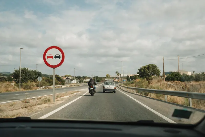 Motocicleta adelantando junto a una señal de prohibido adelantar, sin invadir el sentido contrario
