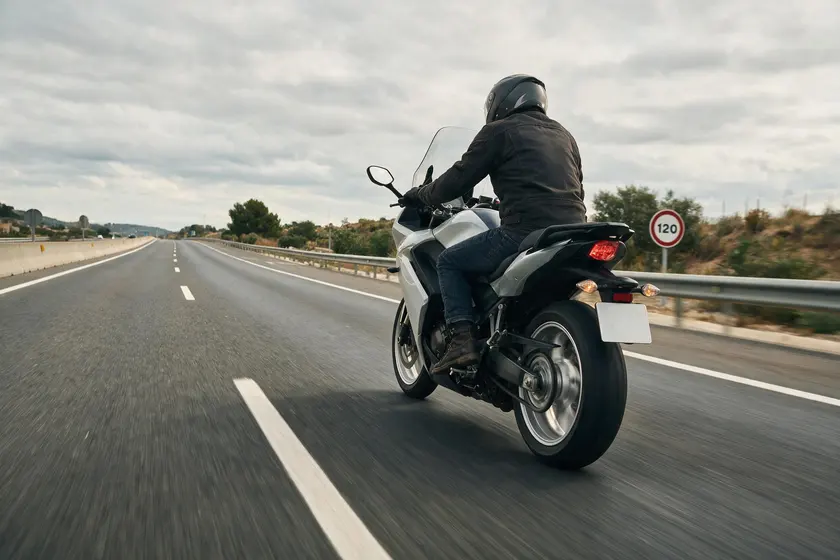 Motocicleta circulando por autopista junto a una señal de límite de 120