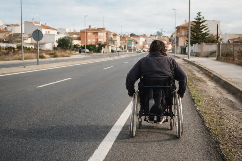 Persona en silla de ruedas circulando por el arcén de una carretera, con acera visible más allá