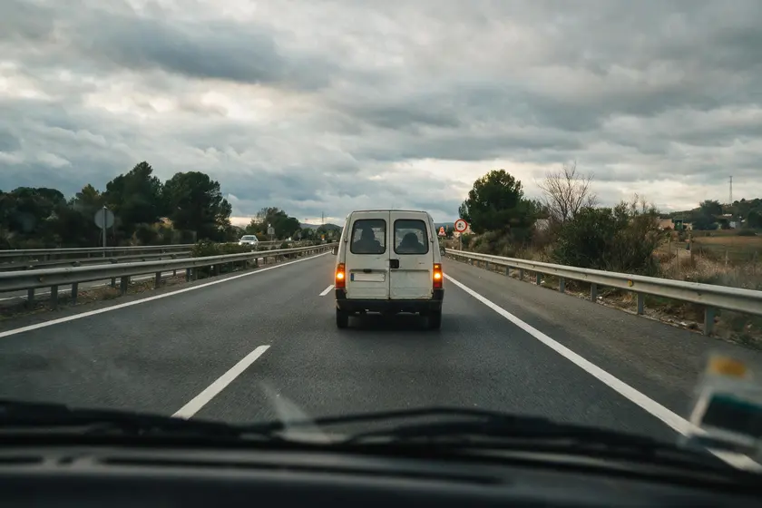 Furgoneta lenta circulando por carretera con los cuatro intermitentes encendidos, vista desde el coche de detrás