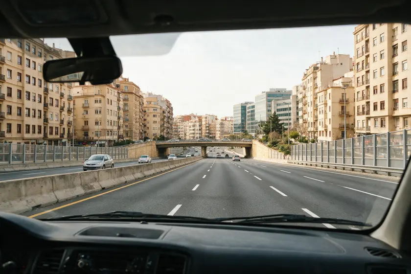 Autovía urbana vista desde el puesto del conductor: varios carriles y barrera central, rodeada de edificios de la ciudad