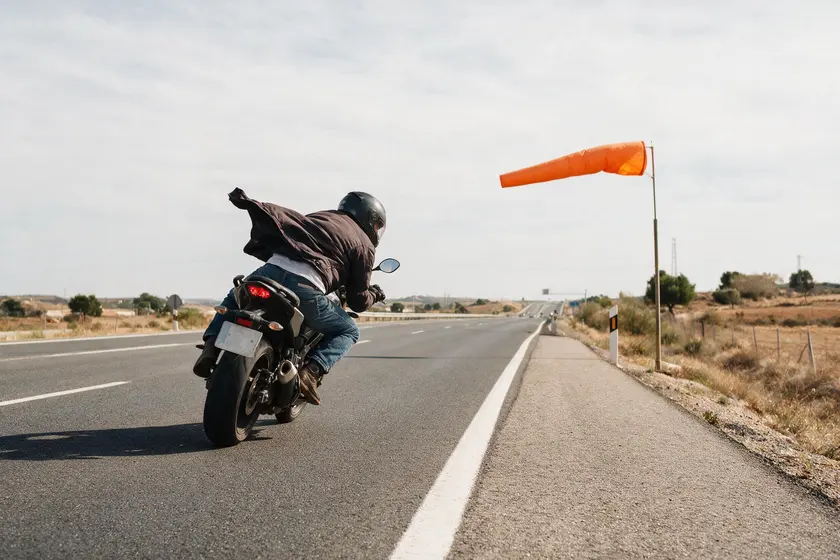 Motorista inclinado por el viento lateral en una carretera expuesta, con la manga de viento horizontal