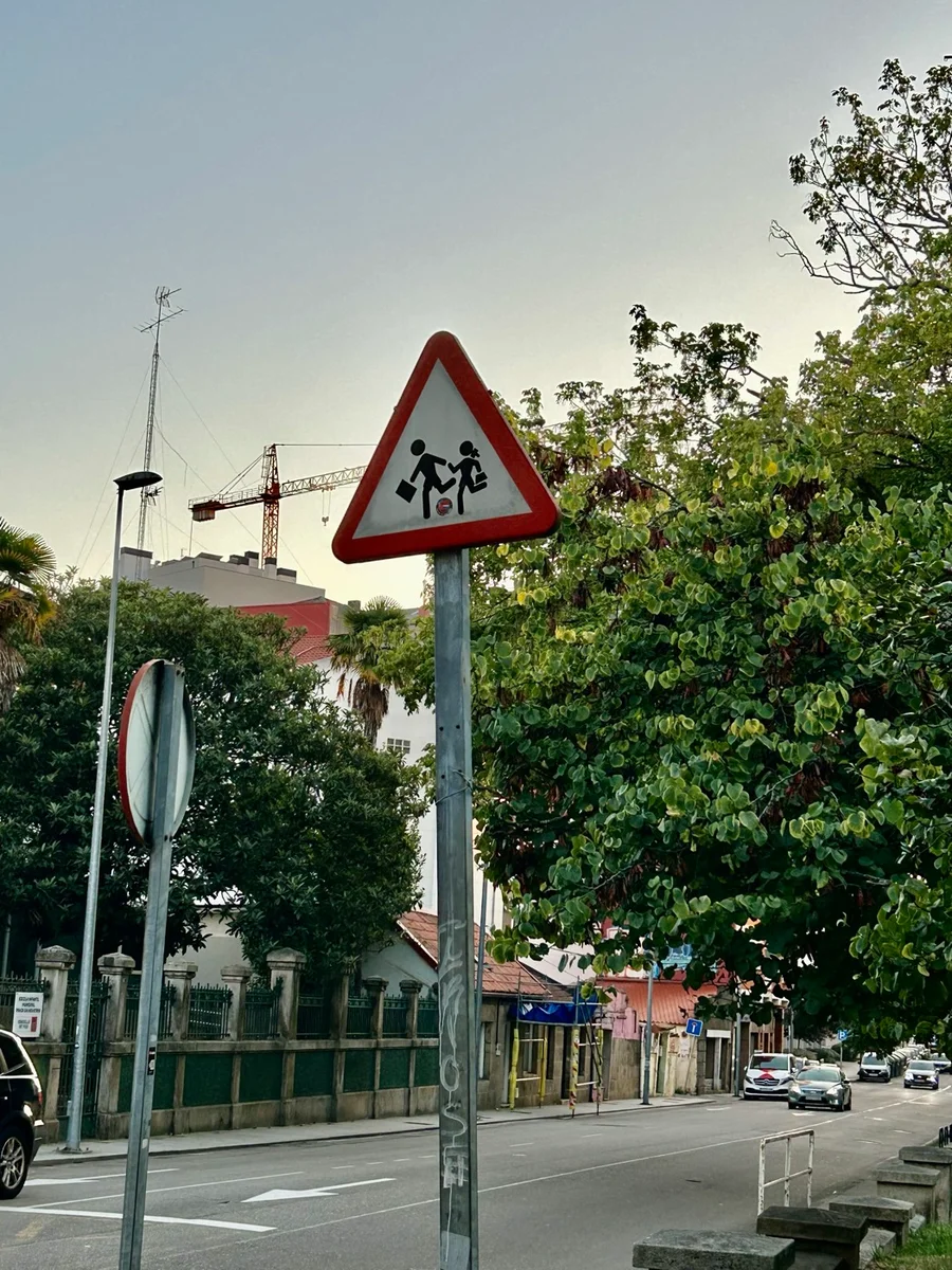 Señal triangular de borde rojo con las siluetas negras de dos niños caminando